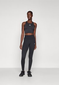Top corto atletico nero e leggings a vita alta con una texture liscia. Logo sul petto e coscia; abbinati a scarpe da ginnastica nere.