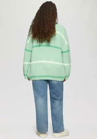 Mintgrüner gestrickter Pullover mit weißen und dunkler grünen Streifen, oversized Passform, kombiniert mit hellblauen Jeans und weißen Sneakers.