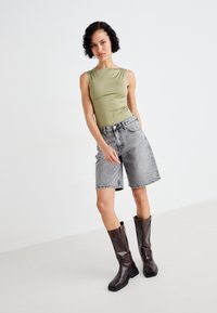 Olivgrön ärmlös topp, högmidjade grå denimshorts och knähöga bruna läderstövlar med fyrkantiga tår. Enkeldesign, inga mönster.