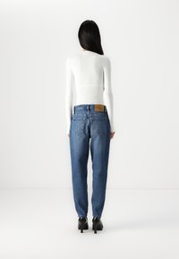 Augstās jostas zilas denima bikses ar brīvu piegriezumu, kurām ir ādas plāksne uz muguras jostas un divas aizmugures kabatas.