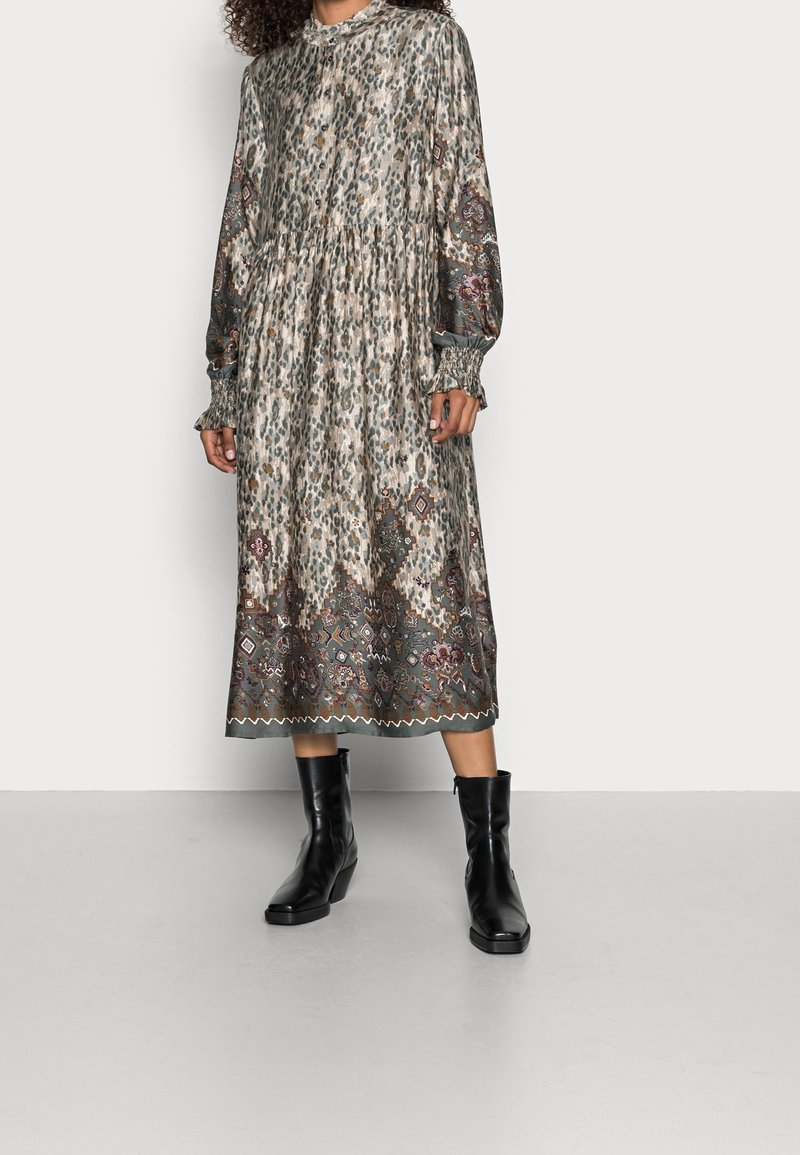 Femme portant une robe midi à manches longues et col montant avec des motifs léopard et géométriques, associée à des bottines noires.