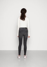 Jeans ajustados negros de cintura alta, con un diseño clásico de cinco bolsillos y costuras en contraste, combinados con una camiseta blanca de manga larga.