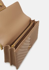 Gestuctureerde beige leren tas met een gequilt ontwerp en gouden hardware. Twee compartimenten, waarvan één met een rits, en afgeronde hoeken.