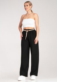 Czarne spodnie z szerokimi nogawkami i elastycznym paskiem z tanowym sznurkiem. Połączone z białym topem crop i białymi sneakersami. Gładka tekstura.