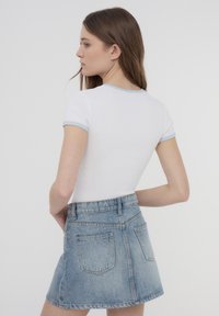 T-shirt bianco aderente con rifiniture azzurro chiaro sul colletto e sulle maniche, abbinato a una mini gonna di jeans azzurro chiaro a vita alta.