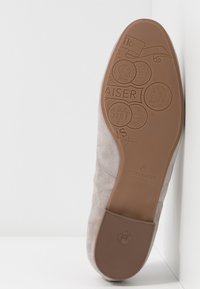 Chaussure en suède gris avec un bout arrondi, semelle en caoutchouc texturé présentant un design en relief et une marque, et un dessus lisse avec des détails de couture.