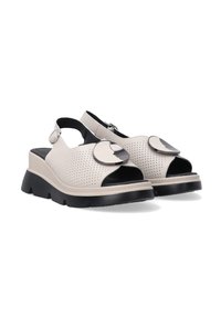 Beige perforerede slingback sandaler med sorte detaljer, chunky sort sål og store runde sølvhardware på forsiden.
