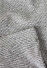 Gråt ribstrikket stof med fine lodrette striber. Indeholder en synlig kant og syet søm. Teksturen fremstår blød og let elastisk.