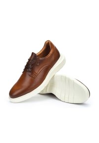 Chaussures en cuir marron au fini lisse, semelles blanches, bout arrondi et détails de couture légers. Les lacets sont foncés, complétant le design de la chaussure.