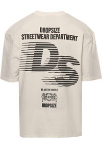 Cream-colored oversized cotton t-shirt featuring bold black text and striped graphics. Back has "DROPSIZE" and "WE ARE THE HUSTLE" prints.