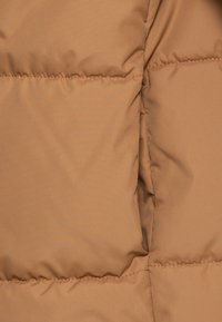 Tessuto di giacca imbottita marrone con sezioni trapuntate, texture liscia e leggero lucido. Presenta cuciture sui punti di giuntura e un'apertura per tasca laterale.