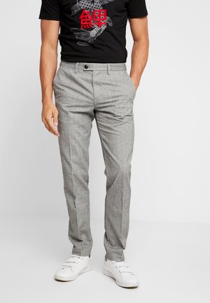 Pantalons rayés gris à coupe ajustée, avec fermeture à bouton et poches, associés à des baskets blanches et un t-shirt graphique noir.