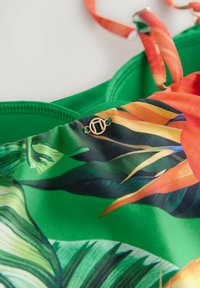 Groene tropical-print stof met oranje en gele accenten; voorzien van lichte gouden hardwaredetails en verstelbare banden.