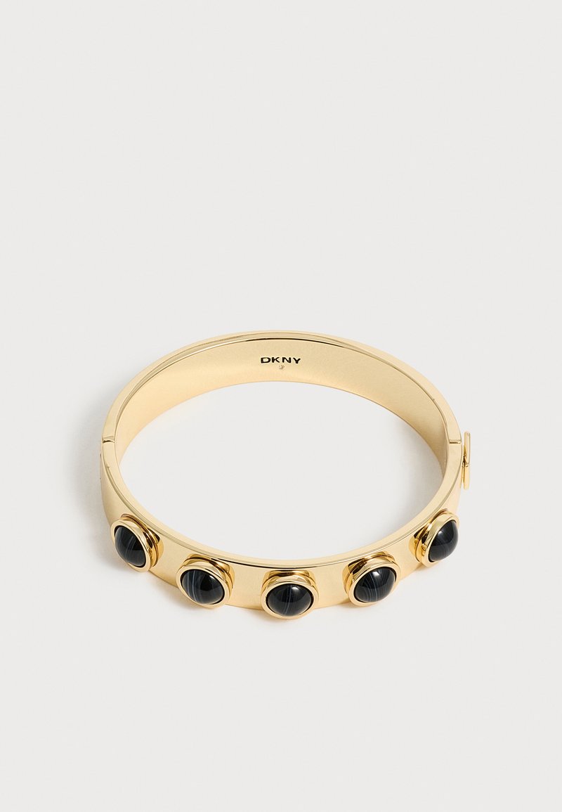 Bracelet jonc doré DKNY avec cinq ornements ronds en pierre noire répartis uniformément sur une surface métallique lisse.