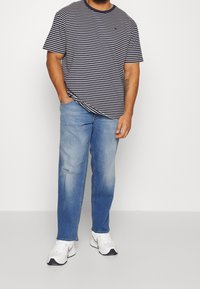 Marinblå och vit randig t-shirt med korta ärmar, kombinerad med ljusblå jeans och vita sportskor. T-shirten har en rund halsringning.