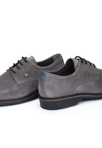 Chaussures en daim gris avec des lacets noirs, bout arrondi et accent de talon bleu. Elles possèdent une semelle en caoutchouc profil bas et un détail de logo subtil.