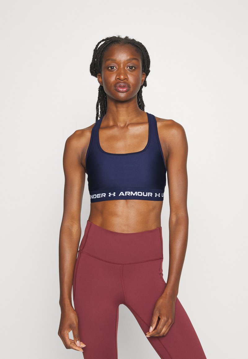 Marineblå sportsbh med hvit "UNDER ARMOUR"-branding, med firkantet utringning og brede stropper, kombinert med høyt midjefede bordeaux leggings.
