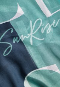 Weiche Stoff in geometrischem Design in den Farbtönen Teal und Marine, mit dem Wort "SunRise" in weißer Schrift über die Oberfläche.
