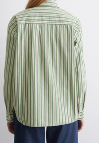 Camisa a rayas con líneas verticales verdes y blancas, con cuello de solapa, puños con botones y un corte relajado, confeccionada con tela suave.