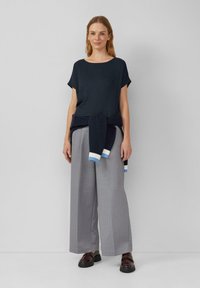 Niebieski sweter z krótkim rękawem, szare spodnie w szerokie paski oraz ciemne buty. Niebieski sweter związany w talii.