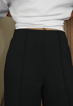 Magas derekú, fekete, testhezálló nadrág, fehér, rövidített felsőt viselő személyen, amely kis részben a meztelen hasat és köldököt mutatja.