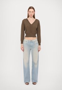Brązowy dzianinowy sweter typu cropped z dekoltem w serek i prążkowanym wykończeniem, zestawiony z jasnoniebieskimi jeansami o szerokich nogawkach z delikatnym wyblaskiem i subtelnym efektem przetarcia.