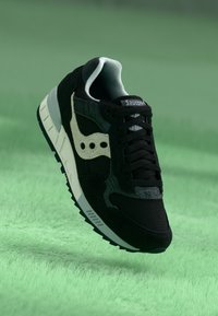Black athletic sneaker featuring a suede and mesh upper, white logo, grey accents, and a white midsole with a textured black rubber outsole.