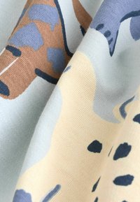 Strikket stof i lyseblå, beige og brun med abstrakte dyremønstre. Blød tekstur med synlige sting og varierede farvepletter.