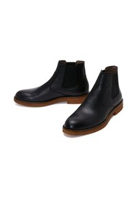 Bottines Chelsea en cuir noir avec finition texturée, panneaux latéraux élastiques et semelles en bois brun. Bout arrondi et design minimaliste.