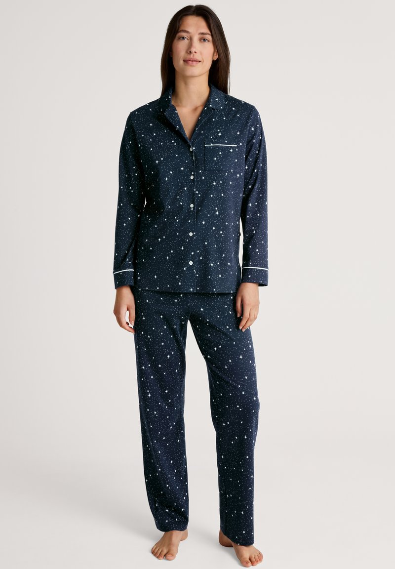 Marineblauwe pyjama set met lange mouwen featuring een sterrenpatroon, witte accenten, een knoopsluiting bovenkant en loszittende broek met een zak.