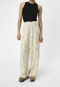Sort ribbet tanktop, brede beige bukser med abstrakte lyse tan mønstre, og brune klipklapper med sølvnitter.