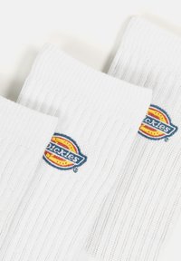 Medias blancas acanaladas con el logo bordado de "Dickies" en azul y amarillo. El diseño tiene una longitud estándar de caña y un tejido texturizado.