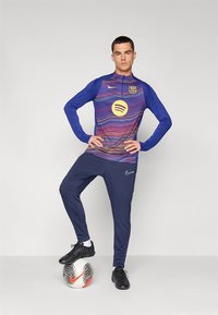 Sinine pika varrukaga särk laineliste mustritega, kollase Spotify logoga ja FC Barcelona vappega, koos tumesiniste pükste ja mustade jalgpallijalatsitega.