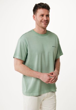 T-shirt en coton vert menthe à manches courtes, col rond et petit logo noir sur la poitrine. Coupe décontractée, texture lisse.