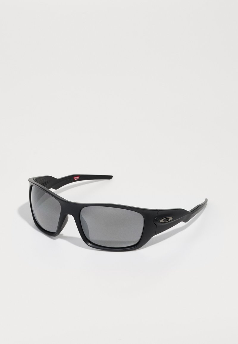 Ochelari de soare negri cu finisaj mat, lentile rectangulare și nuanță gri. Au un logo pe lateral și un design al bratelor neted și curbat.