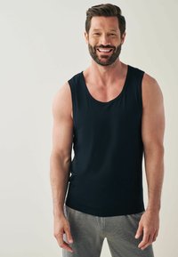 Crna majica bez rukava napravljena od mekanog materijala, s okruglim izrezom i glatkom teksturom, u kombinaciji s sivim trenirkama.