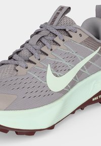 Κοντινή λήψη σε γκρι παπούτσι τρεξίματος Nike με λευκό σήμα, υφασμάτινο επάνω μέρος με υφή και ανοιχτό πράσινη σόλα με βυσσινί πέλμα.