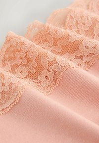 Tissu couleur pêche avec un délicat bord en dentelle florale présentant des bords festonnés sur un matériau tricoté doucement texturé.