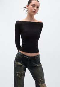 Top negru cu mâneci lungi și decolteu pe umeri, combinat cu blugi întunecați deteriorați, decorați cu ținte metalice și rupturi.