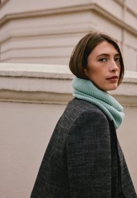 Gray textured blazer with a light blue knitted cowl neck scarf. The scarf has a ribbed pattern and is wrapped around the neck closely.
