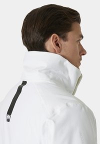 Bílý vysoký límeček s elegantním designem, který má výraznou černou svislou pruh na zadní straně a hladkou texturu.