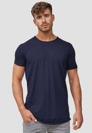 Camiseta de algodón azul marino con cuello redondo y mangas cortas. Presenta un ajuste relajado y una textura sutil. Se lleva con jeans gris claro.
