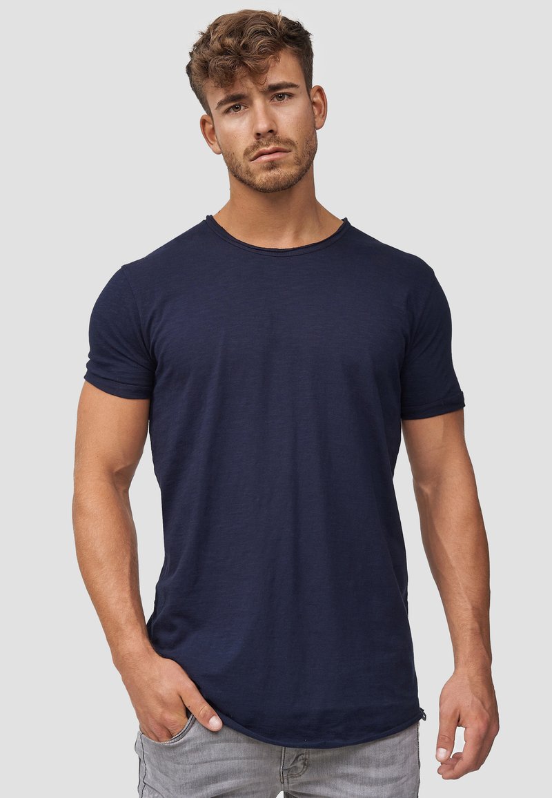 Camiseta de algodón azul marino con cuello redondo y mangas cortas. Presenta un ajuste relajado y una textura sutil. Se lleva con jeans gris claro.