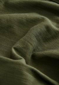Olive green fabric with a soft, textured surface, featuring subtle folds and creases that enhance its drape and fluidity.