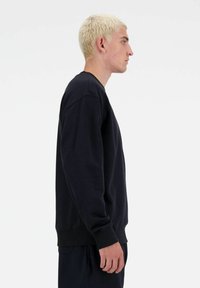 Zwarte sweatshirt met een ronde hals, ribbels aan de mouwen en onderkant. Zachte textuur, relaxte pasvorm. Model wordt in profiel getoond tegen een effen achtergrond.