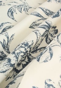 White fabric with a textured surface featuring dark blue floral and leaf patterns, shown in soft folds.