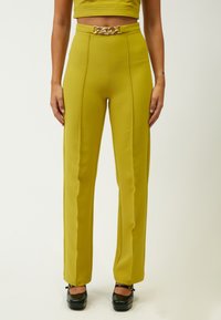 Hoge taille, strakke limoen groene broeken met zijkanten, voorzien van een glanzende gouden kettingriem. Gladde textuur en rechte pijpen.