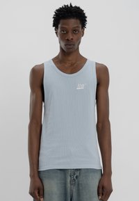 Top de tanque canelado azul-claro com decote arredondado e um pequeno logotipo branco do lado esquerdo. Combinado com calções de ganga desbotados.