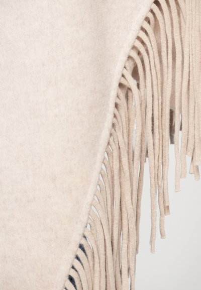 Ljusbeige ullponcho med fransdetaljer längs en kant, med en mjuk textur och en draperad design som är idealisk för lager-på-lager.