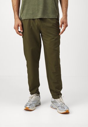 Pantalon léger vert à coupe décontractée avec une légère brillance, associé à des chaussures de sport grises et argentées avec un mesh texturé et des accents orange.